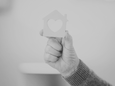 Black and white image of a person holding a house figure with a heart cut out in the middle