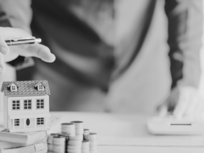 Man with house model on table and stack of coins and paperwork